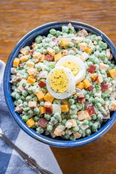 a blue bowl filled with peas, eggs and cheese on top of a wooden table