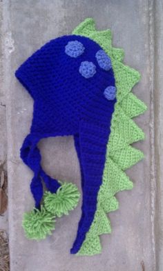 a crocheted blue and green dinosaur hat with pom poms on it