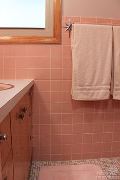 a pink bathroom with two towels hanging on the wall and a window in the background