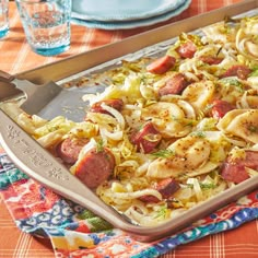 a casserole dish with sausage, onions and cabbage on a colorful table cloth