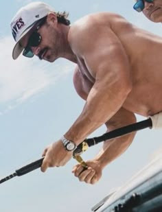 a shirtless man holding a fishing pole while standing next to another man wearing sunglasses