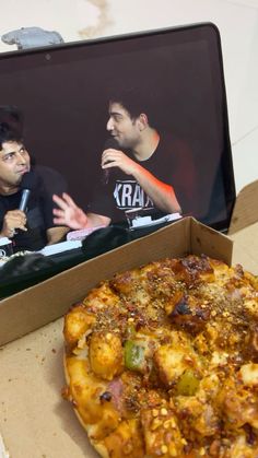 a pizza sitting in a box on top of a table next to a laptop computer