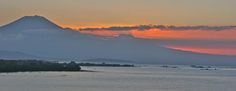 the sun is setting over an island with boats in the water and mountains in the background