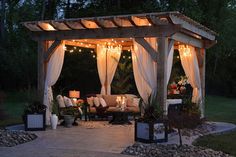 an outdoor gazebo with lights on the top and curtains hanging over it's sides