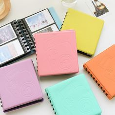 four different colored notebooks sitting next to each other on a white table with pictures in the background