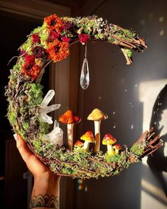 a person holding up a wreath with mushrooms and flowers