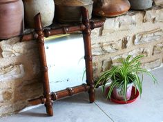 a mirror sitting on top of a wooden shelf next to a potted plant in front of a stone wall