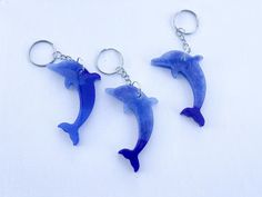 two blue dolphins are hanging from key chains on a white surface, one dolphin has its mouth open and the other is upside down