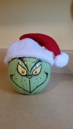 a green pumpkin with a red santa hat on it's head sitting on a counter