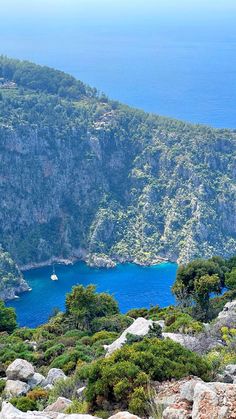 an island with blue water surrounded by trees and rocks in the foreground, on top of a mountain