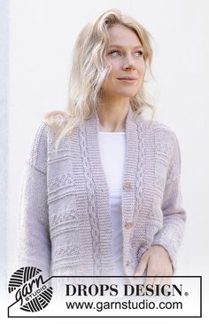 a woman standing in front of a white wall wearing a gray sweater and cardigan