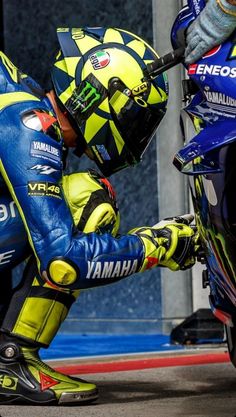 a man in blue and yellow riding on the back of a motorbike next to another person