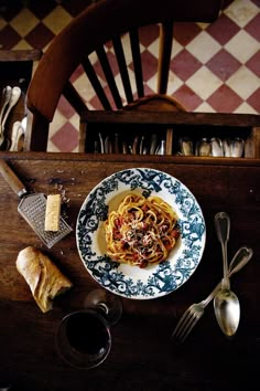 a plate of pasta on a table with bread and utensils next to it