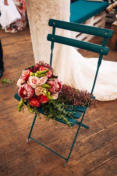 a bouquet of flowers sitting on top of a green chair next to a bride's dress