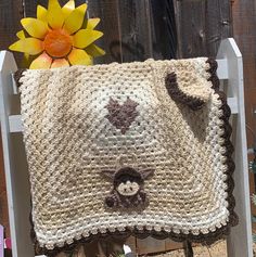 a crocheted monkey blanket sitting on top of a white chair next to a yellow flower