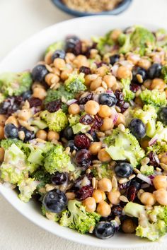 a white bowl filled with broccoli, blueberries and other foodstuffs