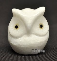 a white owl figurine with black eyes on a gray surface, looking at the camera