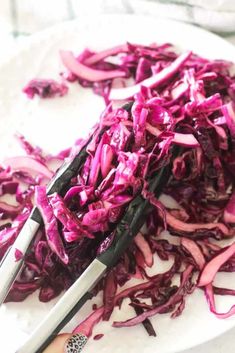 chopped red cabbage on a white plate with tongs