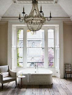 a chandelier hangs from the ceiling over a bathtub in front of two windows