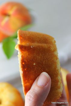 a person holding up a piece of bread in front of an apple and oranges