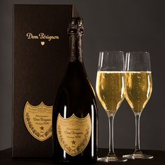 two glasses of champagne next to a bottle and box on a table with a black background