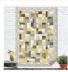 a yellow and gray quilt hanging on a brick wall next to a potted plant