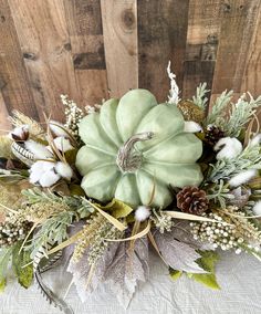 a large green pumpkin sitting on top of a table next to some leaves and flowers