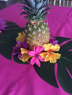 a pineapple sitting on top of a purple table cloth next to flowers and leaves