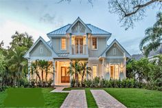 a large white house sitting in the middle of a lush green field with palm trees