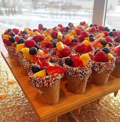 several cones filled with fruit and sprinkles on top of a wooden table