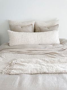 an unmade bed with two pillows on top of it and a white wall in the background