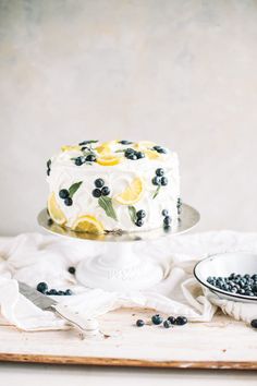 a white cake with blueberries and lemons on it sitting on top of a table