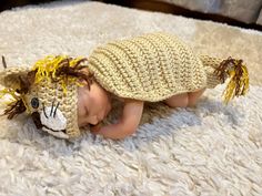 a baby wearing a crocheted lion hat laying on top of a white rug