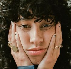 a close up of a person with curly hair and rings on her hands, wearing a blue shirt