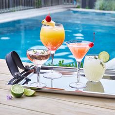 three cocktails on a tray next to a swimming pool