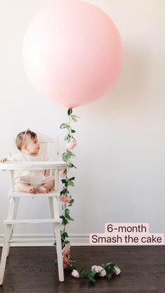 a baby sitting in a high chair with a pink balloon