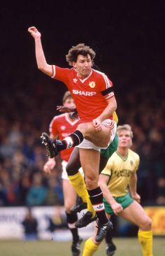 a soccer player jumping up in the air with his foot on the ball while other players look on