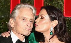 an older man and woman kissing each other in front of a red wall with green curtains