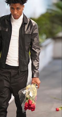 a young man walking down the street with flowers in his hand