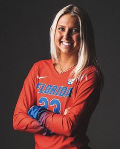 a woman in an orange shirt is posing for a photo with her arms crossed and smiling at the camera