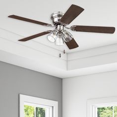 a ceiling fan in a white room with two windows and a light fixture on the ceiling