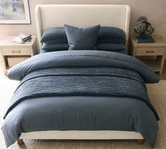 a bed with blue comforters and pillows in a small room next to two nightstands