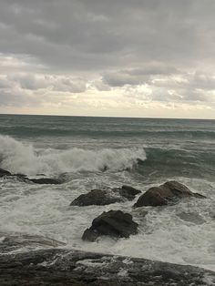 waves crashing on rocks in the ocean under a cloudy sky with white foamy water