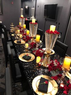 a black table with gold plates and red roses on it is set for a formal dinner