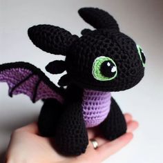 a crocheted black dragon with green eyes sitting on top of a persons hand