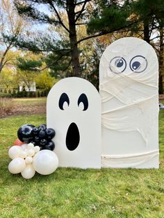 an inflatable ghost next to balloons and a fake pumpkin on the grass outside