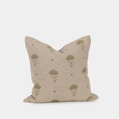 a beige pillow with small green flowers on the front and back, sitting on a white surface