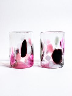 two glass cups with pink and white flowers on them sitting side by side in front of each other