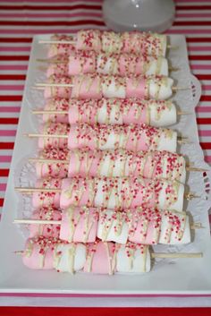 marshmallows and sprinkles are arranged on skewers on a plate