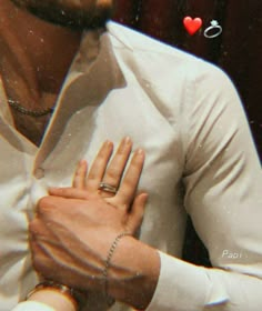 a man wearing a white shirt and holding his hand out to the side, with two hearts in the background